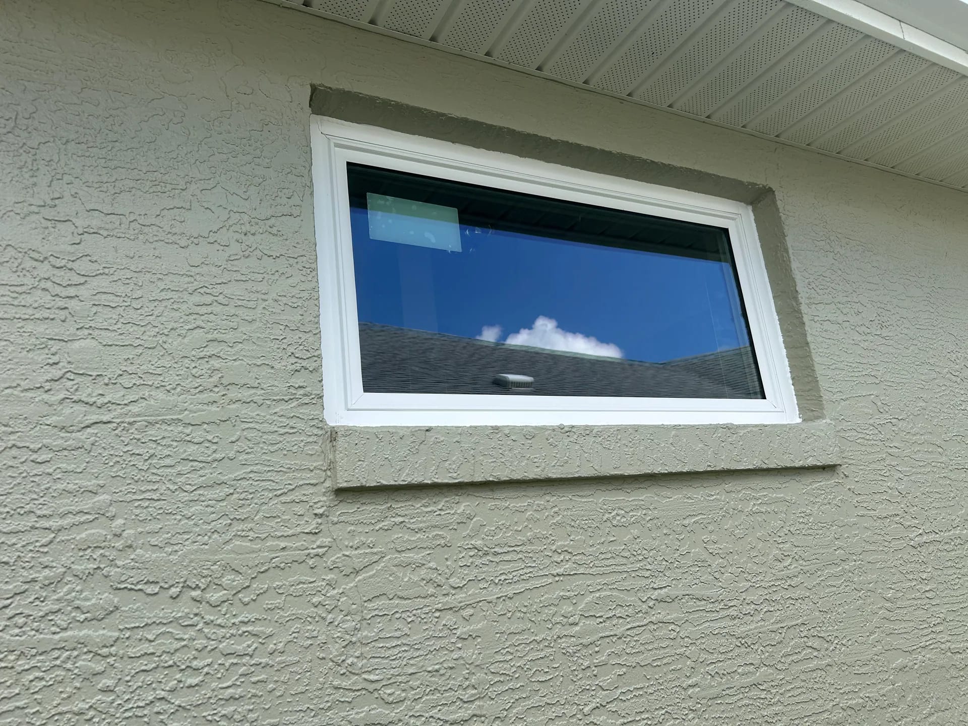 A wide white-framed fixed replacement window installed beneath the eave of a light stucco Central Florida home