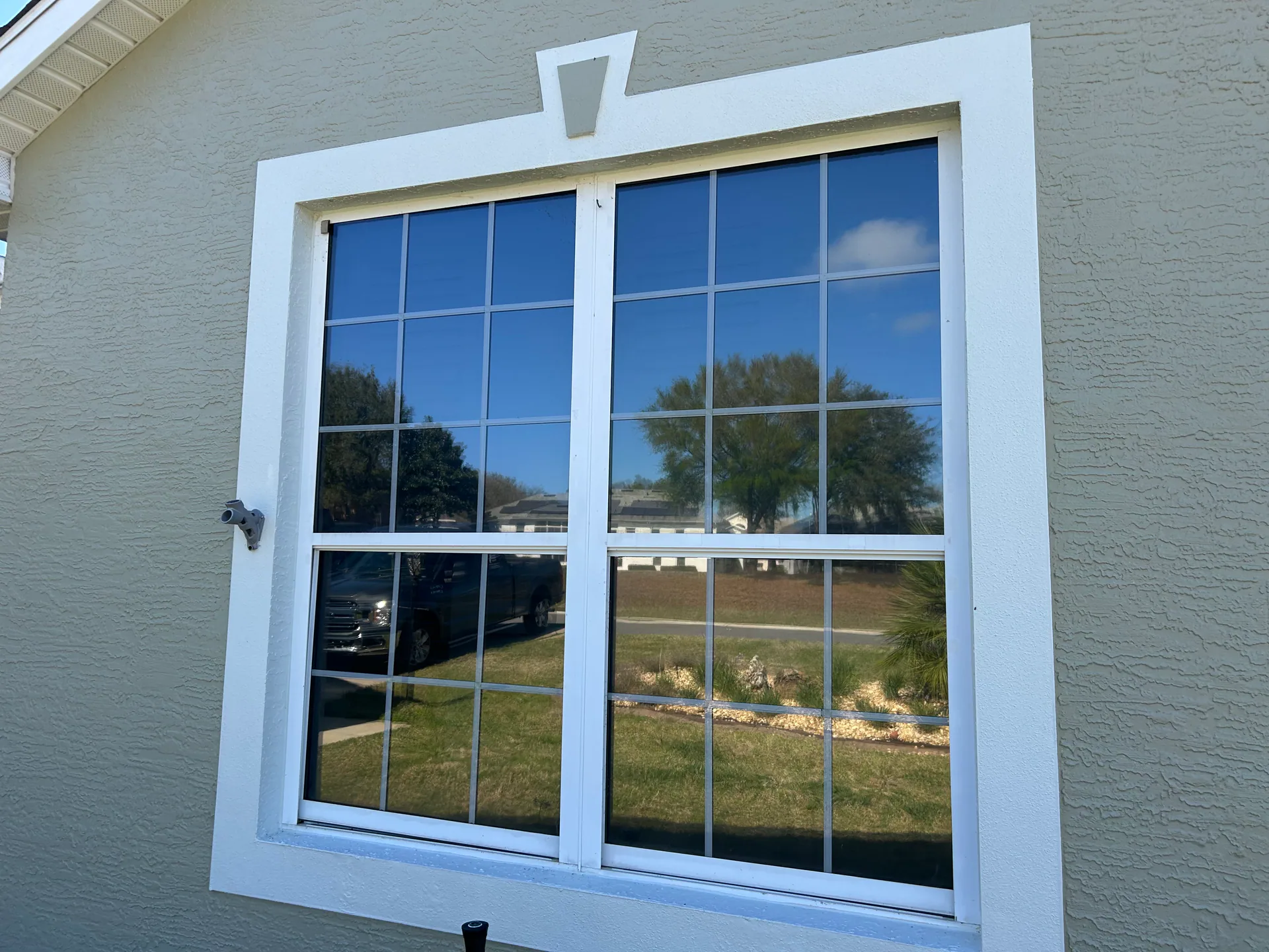 Two white replacement windows with colonial grilles installed side by side in a light stucco Central Florida home