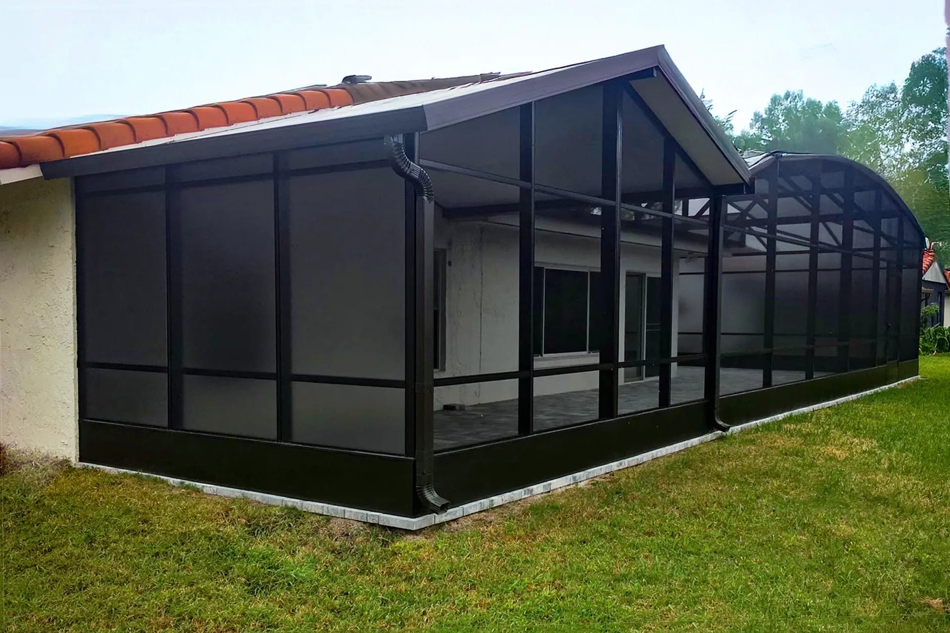 A dark-framed screen enclosure running along a tile-roofed home with a pool cage beyond