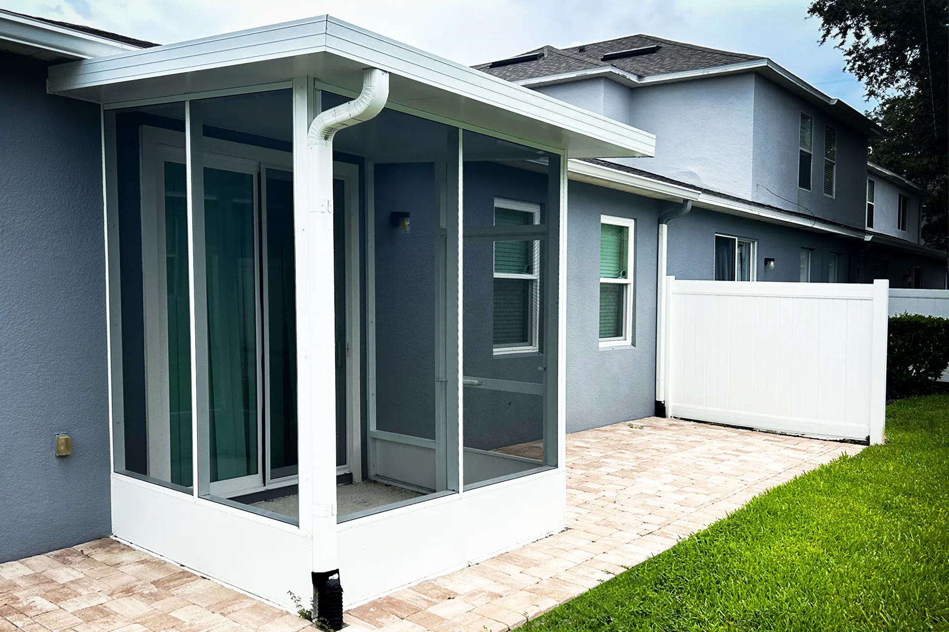 A white-framed screen room built over a paver patio at the rear of a two-storey home