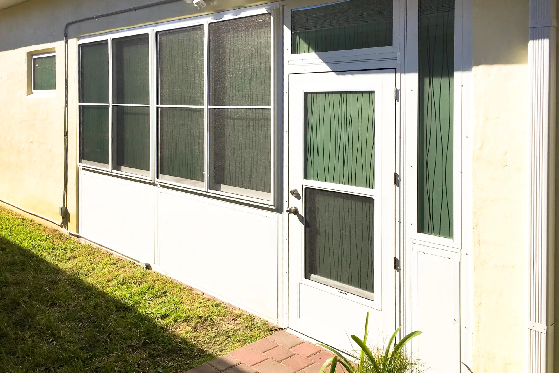 A white-framed screen room with dark screening and a side entry door on a tan Florida home