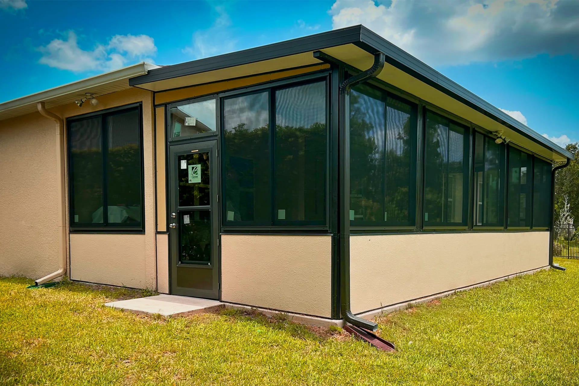 A dark bronze-framed sunroom enclosure spanning the back of a stucco home under a clear blue sky