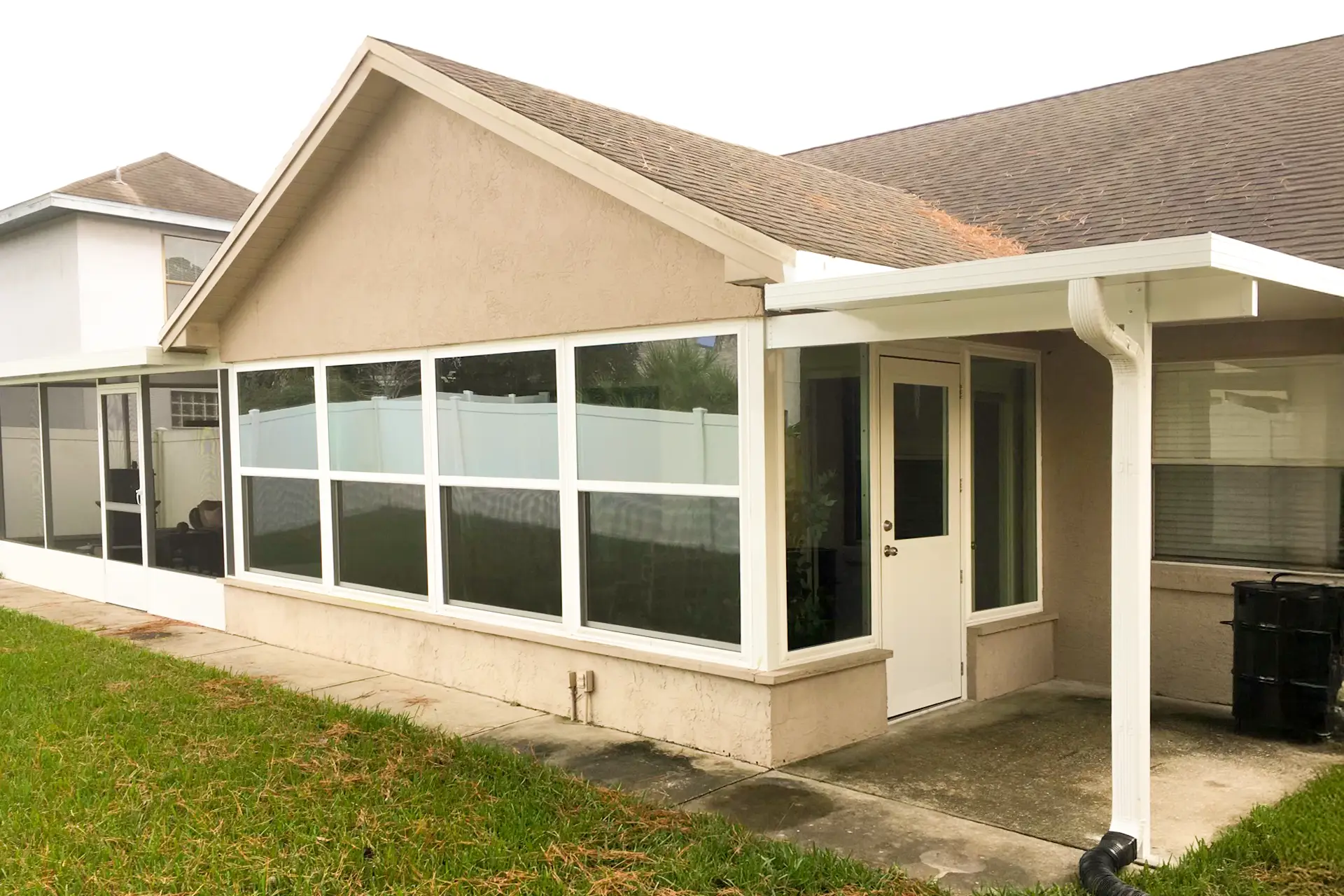 A white-framed sunroom running along the side of a tan Central Florida home, with an entry door beside the carport